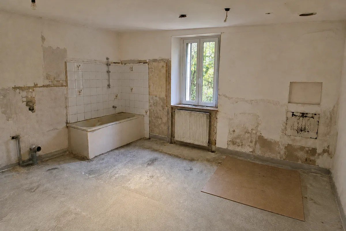 Pièce mise à nu avant travaux : ancienne baignoire, murs piqués et sol d'origine